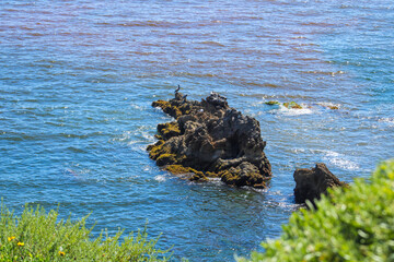 a gorgeous shot of the deep blue ocean water, the lush green hillside and the rock formations of...