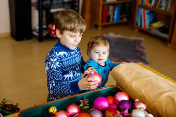 Fototapeta premium Cute baby girl and kid boy taking down holiday decorations from Christmas tree. children, siblings, brother and sister holding vintage toys. Family after celebration remove and dispose tree