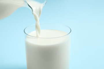 Pouring milk into glass on light blue background, closeup