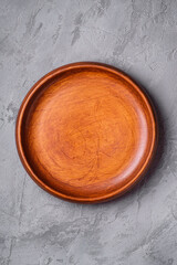 Empty round handcrafted brown wooden plate on stone concrete background, top view