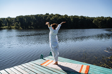 Fototapeta na wymiar a young girl in white clothes does yoga on a pier on a summer Sunny day, yoga asana pose, morning gymnastics, outdoor fitness, sun salute complex
