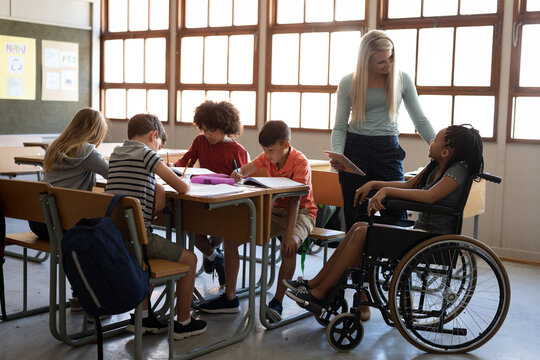 Female teacher with digital tablet talking to a disable girl sitting in her wheelchair at school