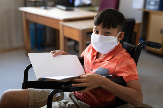 Portrait of disable boy wearing a face mask sitting in his wheelchair at school
