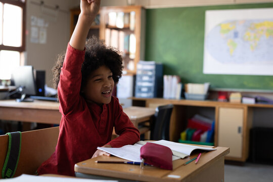 Boy raising his hand while sitting on his desk at school