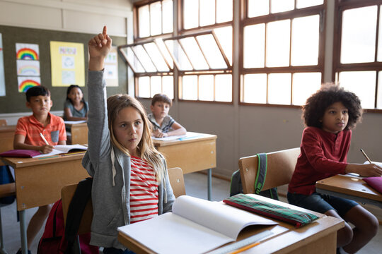 Girl raising her hand while sitting on her desk at school
