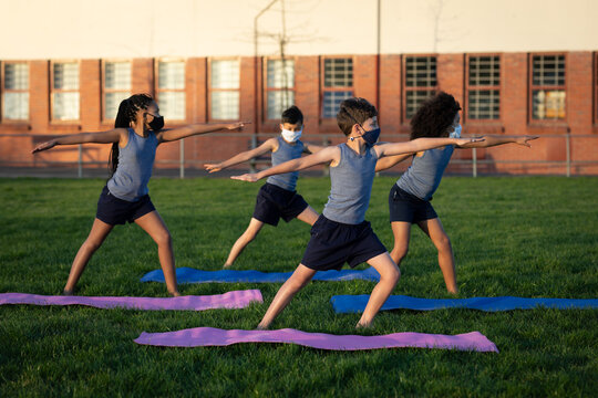 Group of kids wearing face masks performing yoga in the garden
