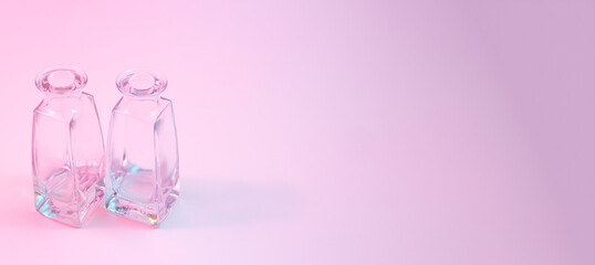 Concept with two shaped square-bottom crystal clear  clean empty glasss bottles standing on colorful background in blue and pink neon vibrant lights. Copy space.
