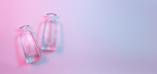 Concept with two shaped square-bottom crystal clear  clean empty glasss bottles laying on colorful background in blue and pink neon lights.