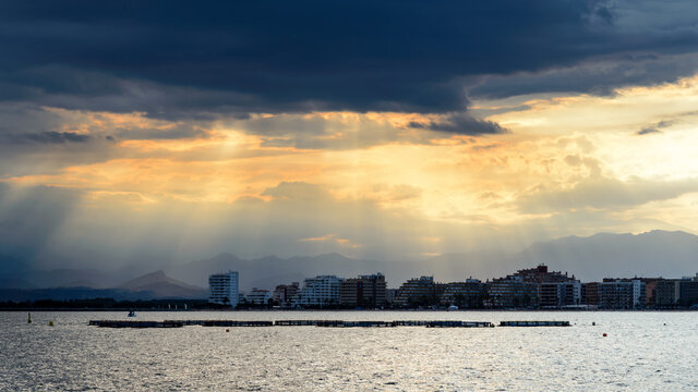 Atardecer en Rosas, Costa Brava:  Nubes de tormenta entre los que se escapan los rayos de sol sobre la silueta de  los edificios de apartamentos de la costa al anochecer 