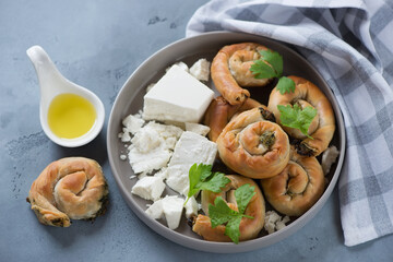 Round grey plate with greek feta and baked mini spiral pies made of filo dough, studio shot on a grey concrete background