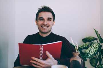 Cheerful young man reading notes in organizer in cafe