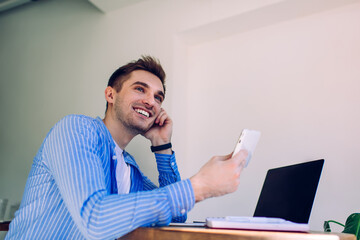 Smiling man using phone while sitting with laptop