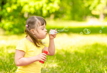 Girl with syndrome down blows bubbles in a summer park
