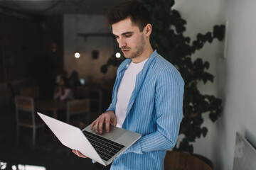 Focused young man standing with laptop in cafe