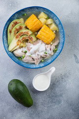 Blue plate with colombian traditional ajiaco soup over light-blue stone background, vertical shot, view from above