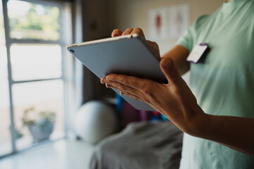 Close up of female physiotherapist scrolling on digital ipad standing in rehab studio.
