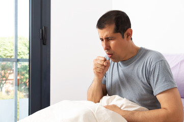 Shot of a handsome young man suffering with thecoughing as symptom for cold or bronchitis while...