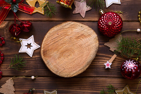 Christmas flat lay of red balloons and wooden stars and clothespins on a dark background with tree trunk section for notes in center. New year's frame, space for text. Xmas toys, beads, pine branches