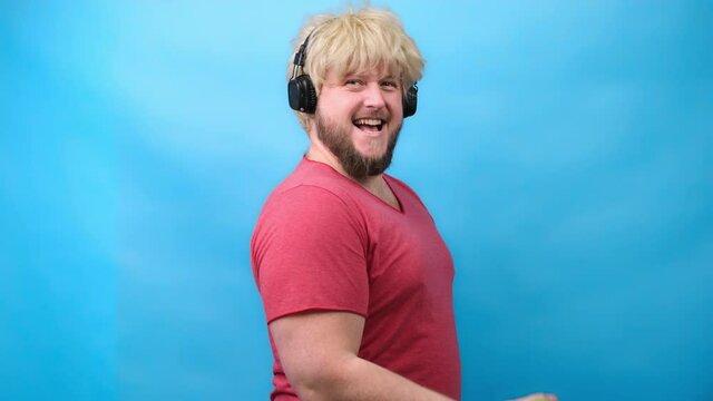 Funny man freaks in headphones and with a haircut from 70 sin pink T-shirt deals with small green dumbbells and smiles
