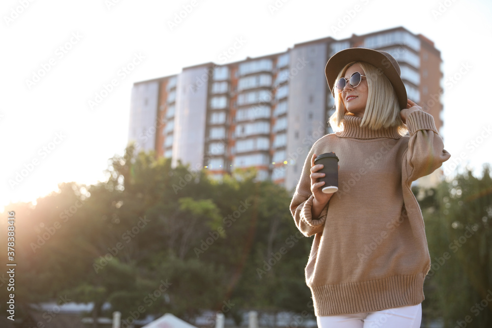 Poster Woman in stylish sweater with cup of coffee on city street