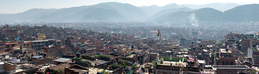 Bhaktapur, Kathmandu, Nepal - December 23, 2019: Panoramic cityscape view from a roof top over brick houses and temples with unidentified people, their gardens, plants and laundry on the roofs