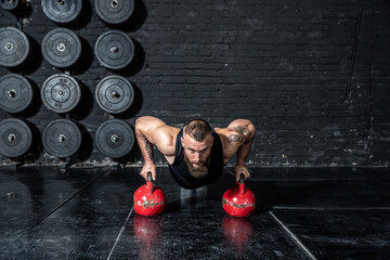 Young sweaty strong fit muscular man with big muscles doing push ups on the kettlebells in the gym as hardcore cross workout training