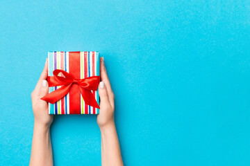 Woman arms holding gift box with colored ribbon on blue table background, top view and copy space...