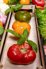 Close up fresh ripe farm tomatoes - red, green and yellow in small wooden box on table. Vertical orientation, perspective view. Advertising healthy natural food. Vegetable harvest. Real organic food.
