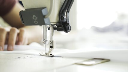 Sewing on machine, hands and white cloth close up. Sewing on digital machine, power button, female hands on white machine with blurry background