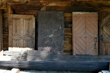 Close up on a set of old medieval decorative doors standing next to a wooden barn made entirely of planks, logs, and boards with a small wooden bench made out of a hollowed out tree seen in Poland