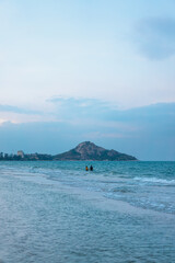 The waves hit the coast in the evening. A woman and a man were Hands in hand together in the middle of ocean. The background has an island with a clear sky in the soft. There is a copy space.