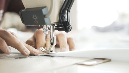 Hands and white cloth close up, sewing on machine. Digital machine, power button, female hands on white machine with white blurry background