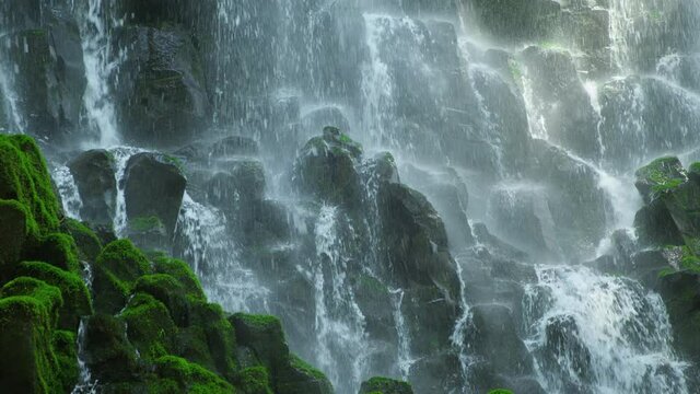 Waterfall cascades over mossy rocks in slow motion, low angle