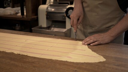 Male hands cutting dough rolled on big wooden table at the restaurant kitchen. Making ravioli, cutting big long slice of raw dough, italian cuisine