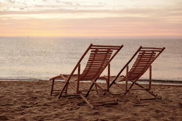 Wooden deck chairs on sandy beach at sunset. Summer vacation