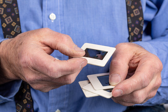 an elderly man hands holding 35 mm slides of old photographs in his rough hands suggesting memory