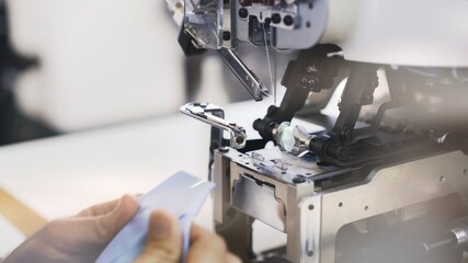 Sewing on machine, needle and hands with and blue cloth close up. Sewing process, female hands getting blue cloth to a modern white machine blurry shot