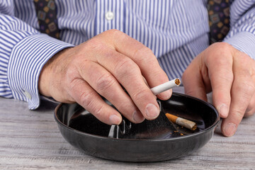 an elderly man's hands holding an un lit cigarette over an ash tray