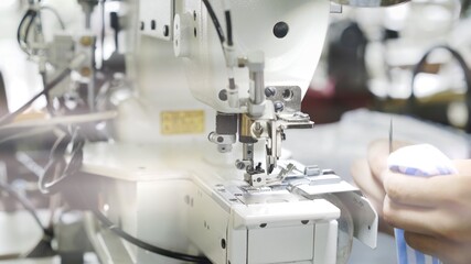 Sewing on white machine, hands and blue and white striped cloth close up. Sewing process, female hands on white machine, modern sewing machine on studio background lens flare