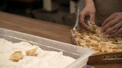 Male hands in flour on several tortellini in the tray with flour. Preparation of italian food at the restaurant kitchen, cook laying italian tortellini on wooden tray