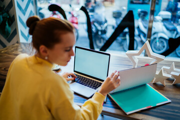 Fototapeta na wymiar Woman reading notebook and browsing laptop at cafe
