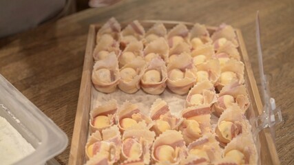 Tortellini in rows on a wooden tray close up, top view shot, on wooden kitchen table at the restaurant kitchen. Cooking italian food, handmade tortellini
