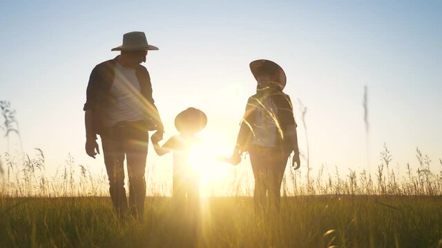 Happy Family Dad Mom And Son Walk Lifestyle On The Field Holding Hands Teamwork Silhouette At Sunset. Happy Family Together Parents Father Mother And Boy Kid Are Walking On The Grass