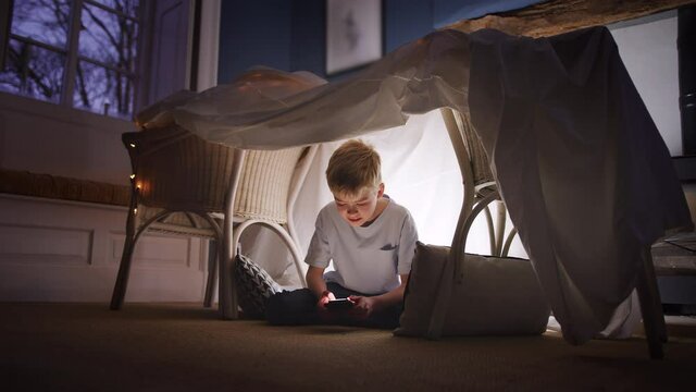 Boy sitting in den or camp he has made at home playing with mobile phone - shot in slow motion