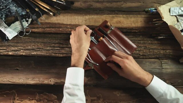Male painter opens leather case with tools, brushes, Palette knife