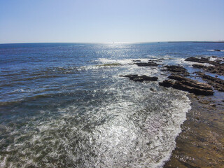 gorgeous aerial shot of the waves and the deep blue ocean water and the large rocks on the beach...