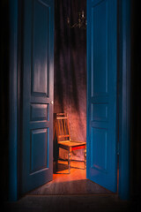 Fototapeta na wymiar empty chair in light behind blue massive vintage doors indoor. Old fashioned interior concept 