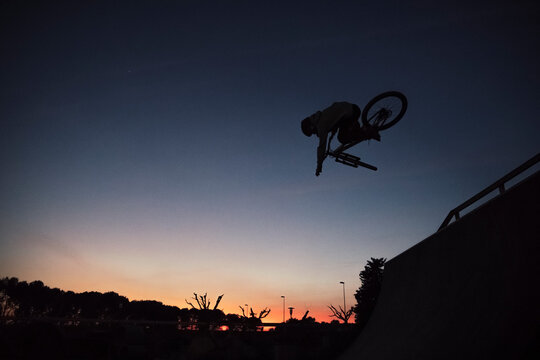 Silhouette young man performing stunt with bicycle against clear sky during sunset