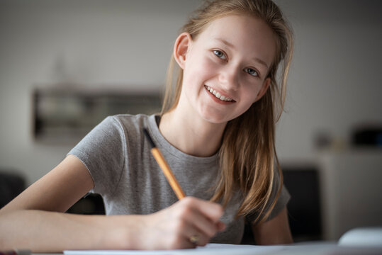 Smiling girl learning at home, writing in exercise book