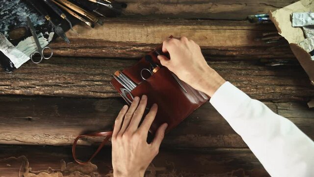 Male painter opens leather case with tools, brushes, Palette knife